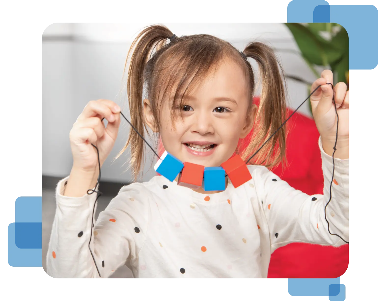 A preschool girl holds up a string of wooden blocks.