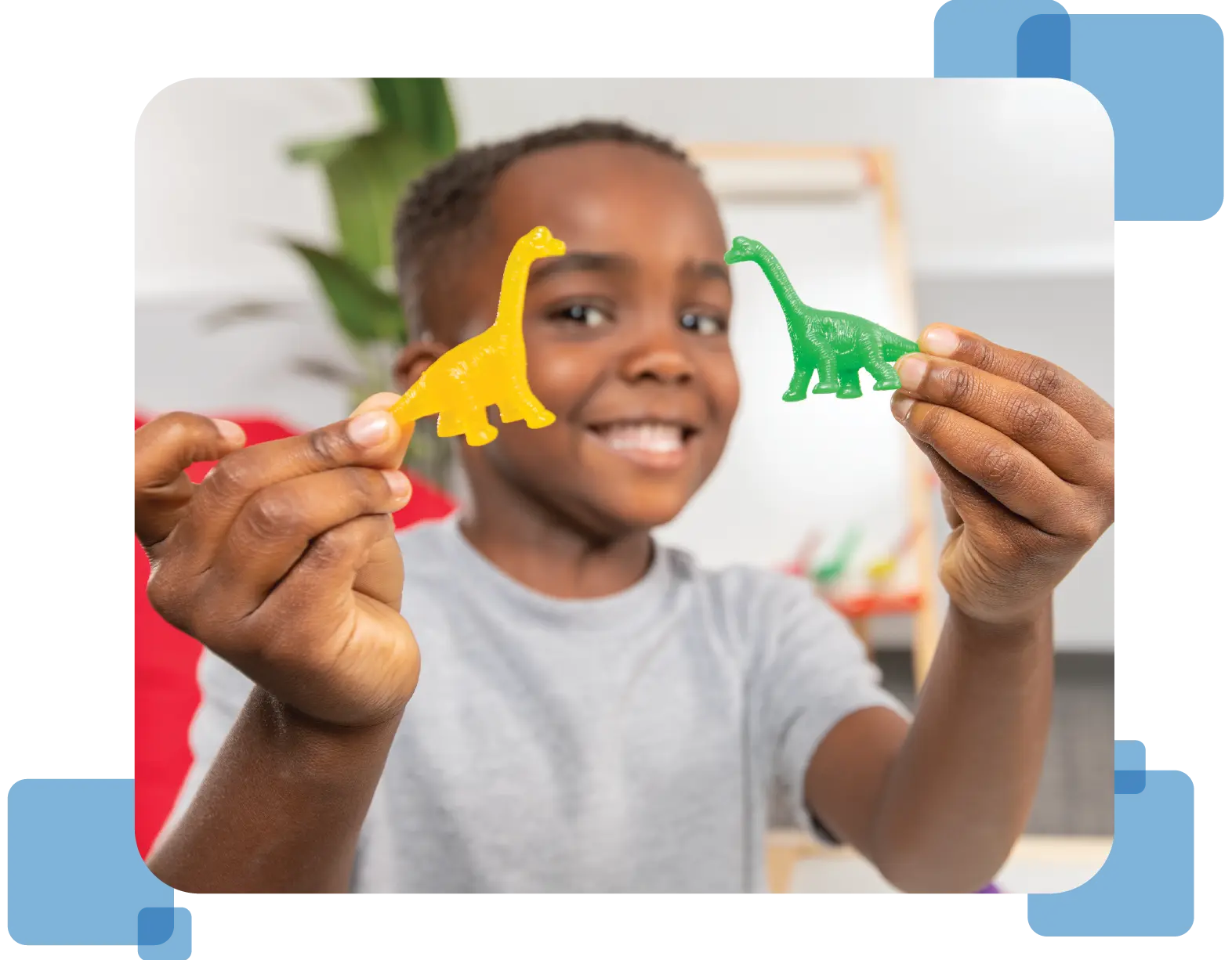A young child holds up a long-necked dinosaur figurine from the  program’s Manipulative Kit in each hand.