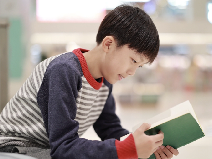 A young student grins while reading a book.