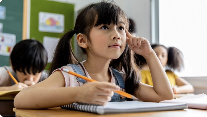 A student looks up from their desk  while holding a pencil in their hand.