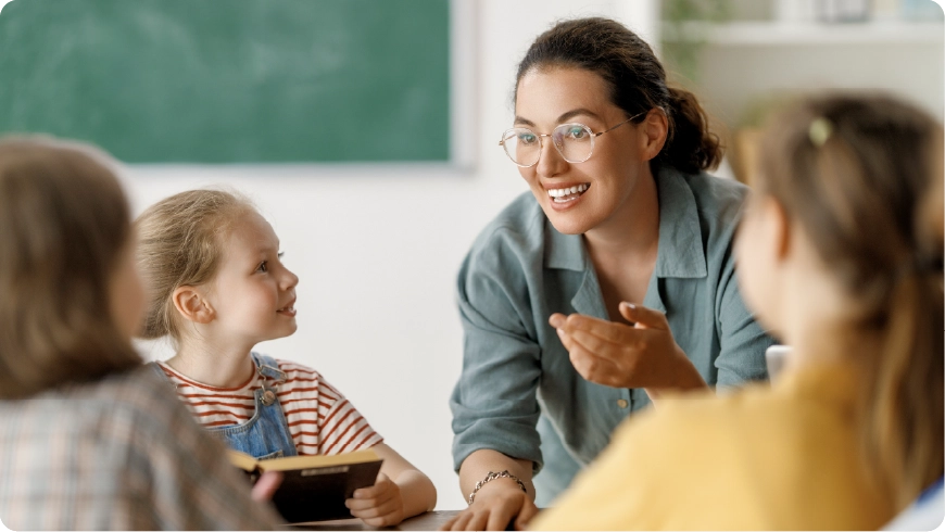 A teacher smiles at their students in a classroom.
