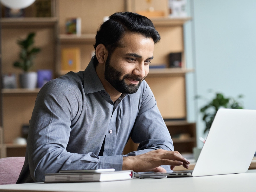 A man at a desk clicks a button on a laptop.