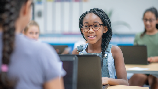 A student wearing glasses looks up from her laptop at her desk.