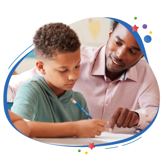 From Humble Beginnings: A teacher looks over a student’s shoulder as he writes.